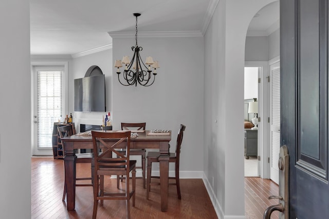 dining room featuring crown molding, arched walkways, an inviting chandelier, and wood-type flooring