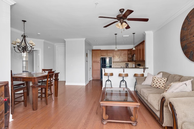 living room with light wood-style floors, baseboards, ornamental molding, and ceiling fan with notable chandelier