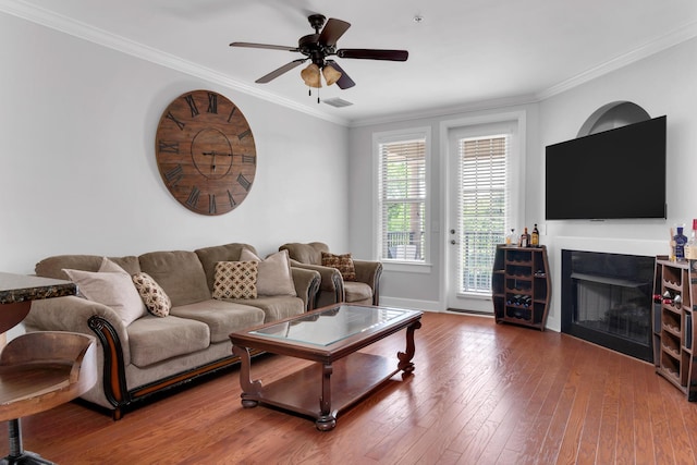 living area with crown molding, a glass covered fireplace, a ceiling fan, visible vents, and hardwood / wood-style flooring