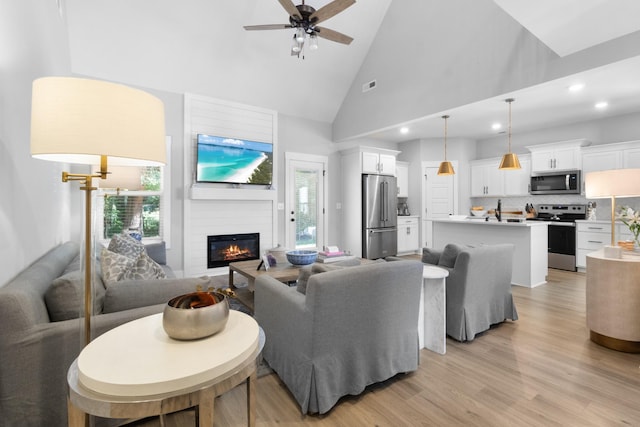 living area featuring a ceiling fan, a large fireplace, high vaulted ceiling, light wood-style floors, and recessed lighting