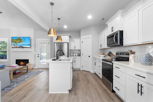 kitchen featuring appliances with stainless steel finishes, a sink, a fireplace, decorative backsplash, and visible vents