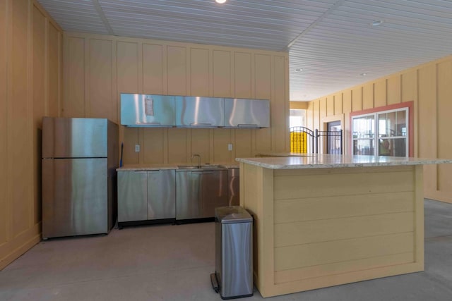 kitchen featuring light stone counters, freestanding refrigerator, and a sink