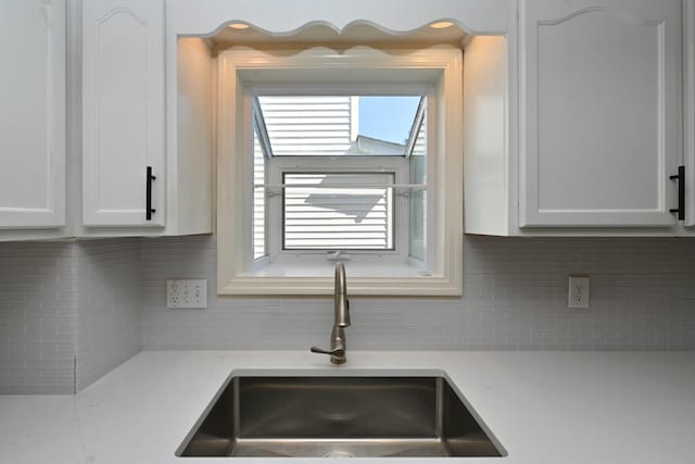 details featuring light countertops, a sink, white cabinets, and tasteful backsplash