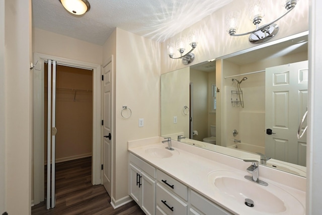 full bathroom with a sink, double vanity, toilet, and wood finished floors
