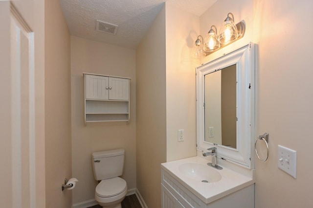 bathroom with vanity, toilet, a textured ceiling, and visible vents