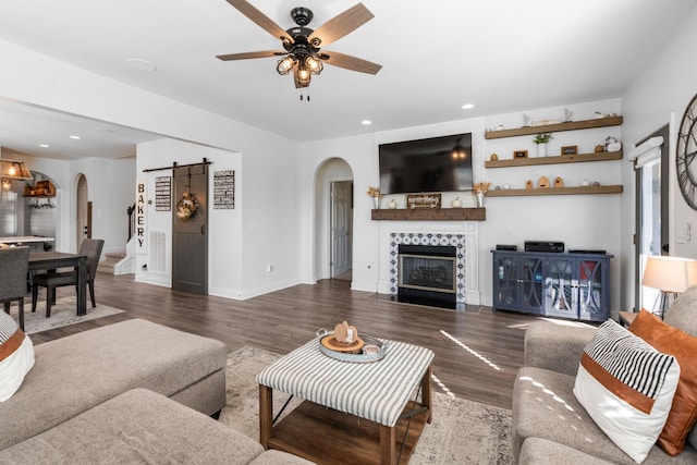 living area with a ceiling fan, arched walkways, a fireplace, a barn door, and wood finished floors