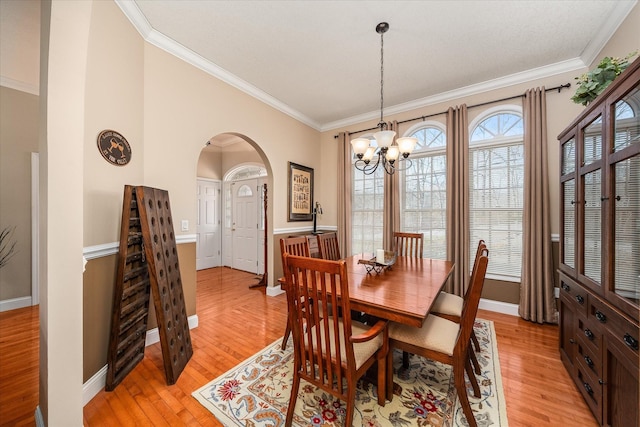 dining space with crown molding, an inviting chandelier, light wood-style floors, arched walkways, and baseboards