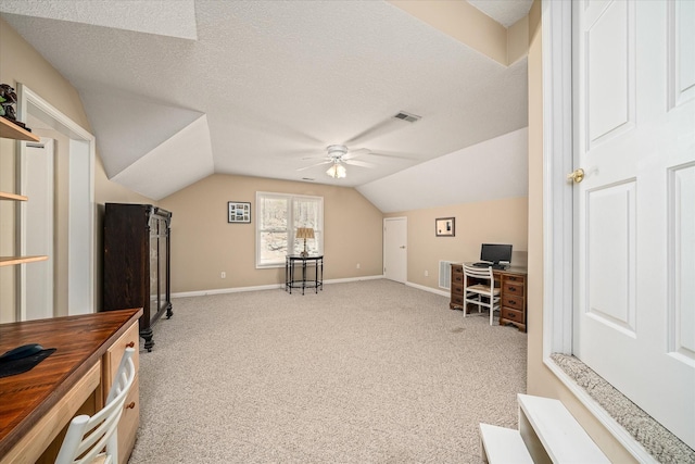 home office featuring visible vents, light carpet, a textured ceiling, a ceiling fan, and vaulted ceiling
