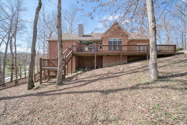 rear view of property featuring a chimney, a deck, brick siding, fence, and stairs