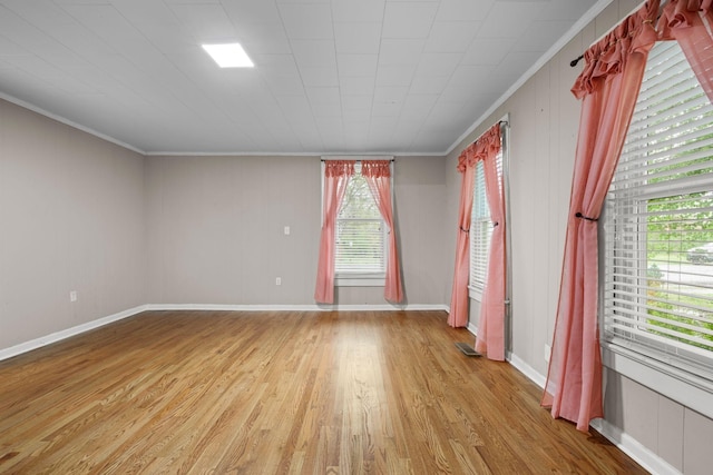 empty room featuring crown molding, light wood finished floors, baseboards, and visible vents