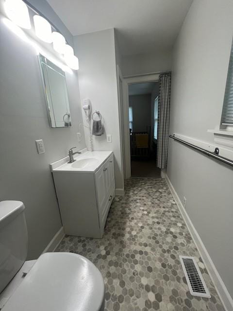 half bath featuring baseboards, vanity, toilet, and visible vents