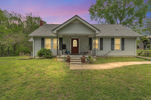 ranch-style house featuring a porch, roof with shingles, a yard, and a chimney