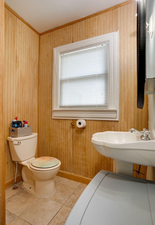half bath with wood walls, ornamental molding, toilet, baseboards, and tile patterned floors
