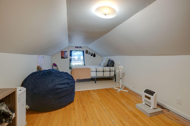 bedroom featuring light wood-style floors, heating unit, baseboards, and vaulted ceiling