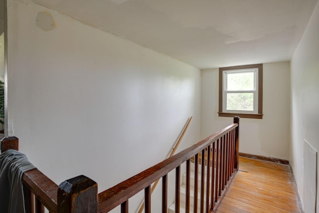 corridor with baseboards, light wood finished floors, and an upstairs landing