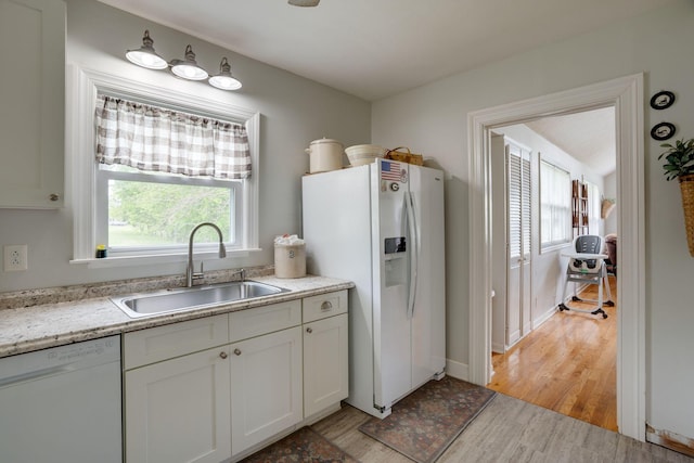 kitchen with a sink, plenty of natural light, light wood finished floors, and white appliances