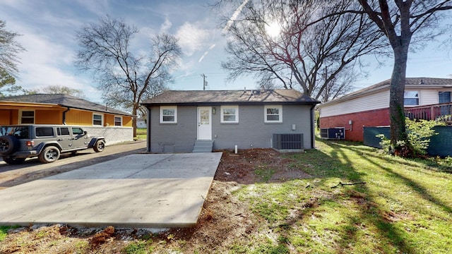 rear view of house with entry steps, a yard, central AC, and brick siding