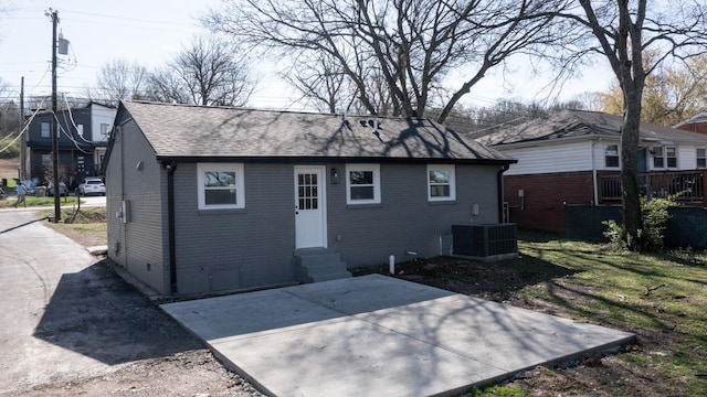 rear view of property with entry steps, a shingled roof, a patio area, and brick siding