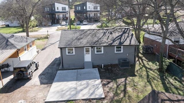 back of house featuring central AC, roof with shingles, brick siding, entry steps, and a residential view