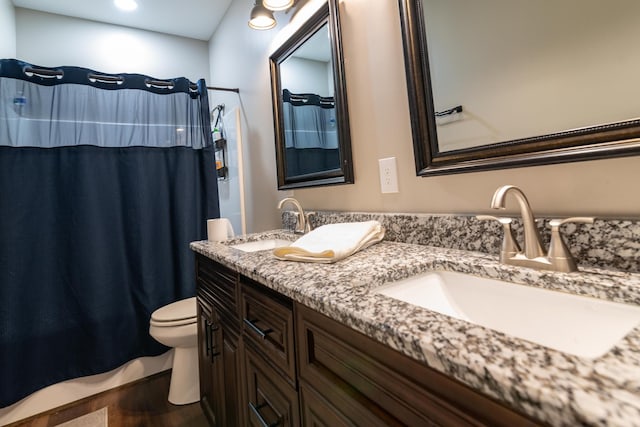 bathroom featuring double vanity, a sink, wood finished floors, and toilet