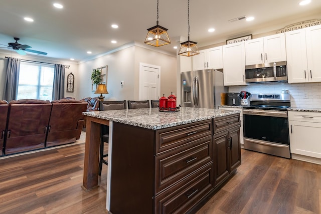 kitchen with a breakfast bar area, visible vents, appliances with stainless steel finishes, open floor plan, and ornamental molding