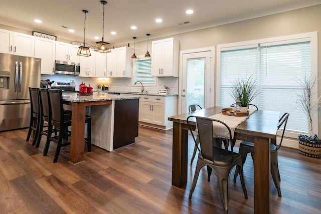 kitchen featuring white cabinets, appliances with stainless steel finishes, a sink, decorative backsplash, and a kitchen island