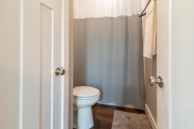 bathroom with wood finished floors, toilet, and a shower with curtain