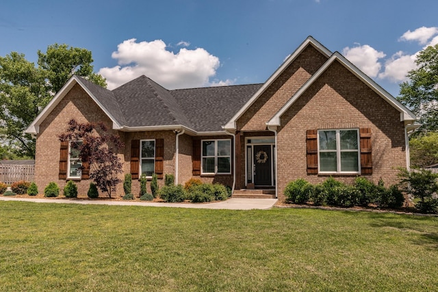 view of front facade featuring a shingled roof, a front yard, and brick siding