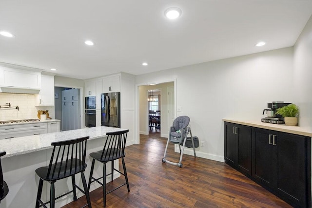 1121 Walnut Grove Church Rd, Dayton, TN 37321 - kitchen with dark wood finished floors, decorative backsplash, a kitchen bar, under cabinet range hood, and black appliances