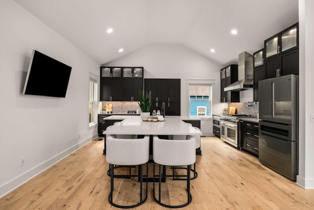 kitchen featuring light countertops, dark cabinetry, wall chimney exhaust hood, freestanding refrigerator, and double oven range