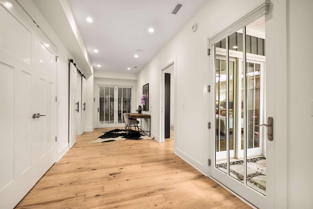 hall with a barn door, recessed lighting, baseboards, light wood-type flooring, and visible vents