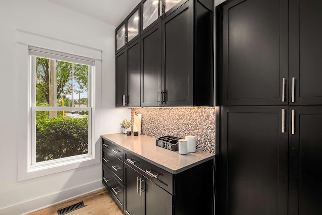 bar featuring visible vents, light wood-style flooring, baseboards, and tasteful backsplash