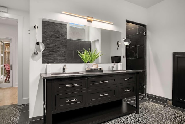 full bath featuring a sink, baseboards, tiled shower, and double vanity