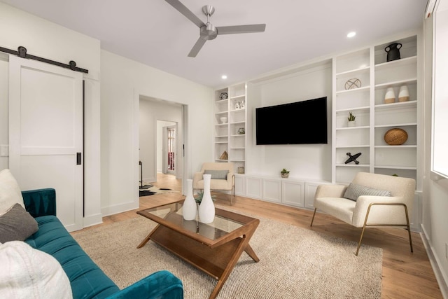 living area with ceiling fan, a barn door, light wood-style floors, built in features, and baseboards