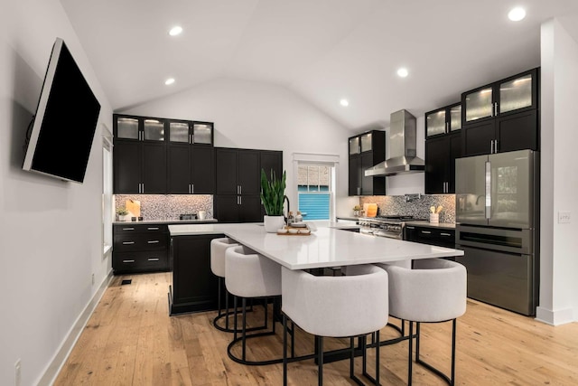kitchen with appliances with stainless steel finishes, light countertops, dark cabinets, wall chimney exhaust hood, and backsplash