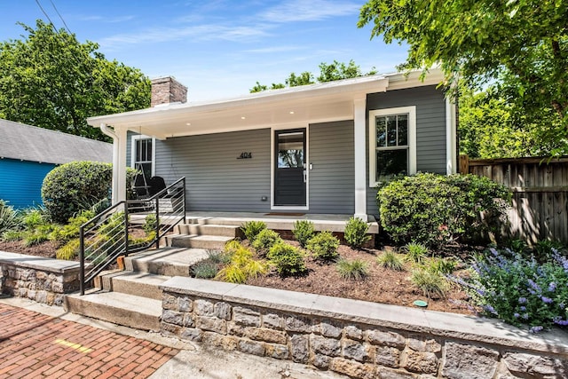 bungalow-style house featuring covered porch, fence, and a chimney