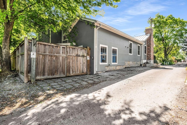 view of side of property featuring fence, metal roof, a chimney, and a standing seam roof