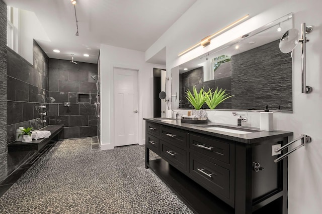 bathroom with double vanity, a sink, a tile shower, and tile walls