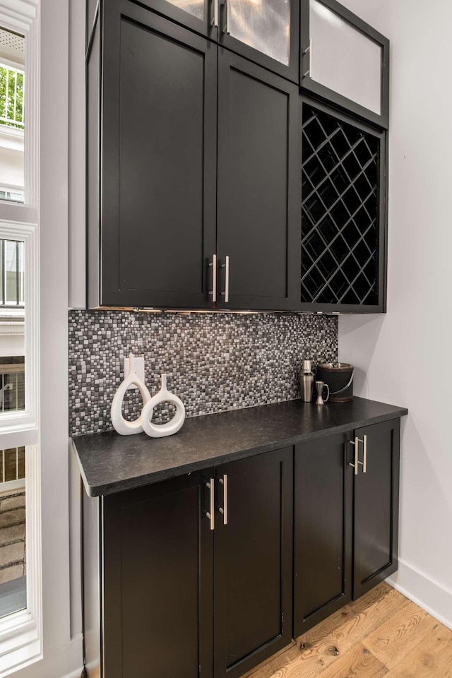 bar with light wood-style floors, a dry bar, decorative backsplash, and baseboards