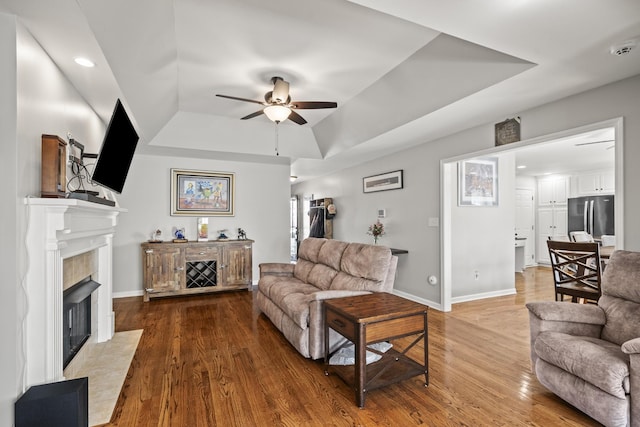 living room with a ceiling fan, a tray ceiling, wood finished floors, and a high end fireplace
