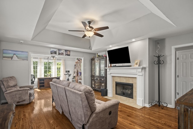 living room featuring a raised ceiling, a ceiling fan, a tile fireplace, and wood finished floors