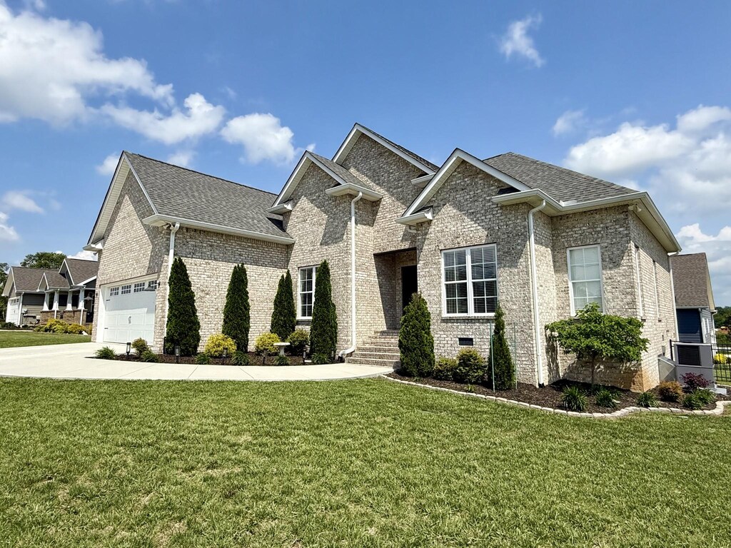 french provincial home with a shingled roof, driveway, brick siding, and a front yard