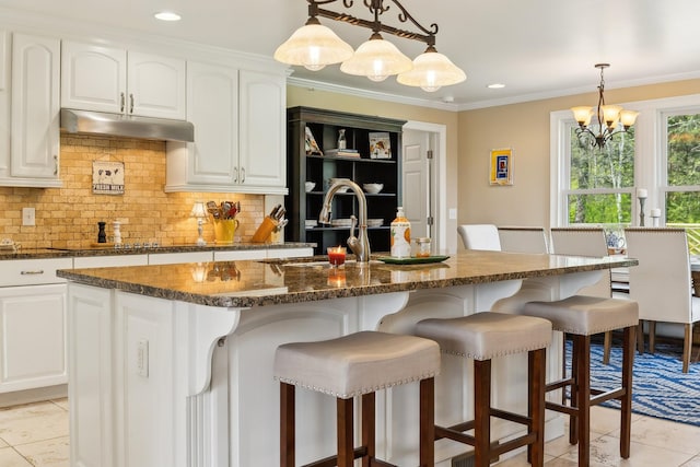 921 Cooks Rd, Mount Juliet, TN 37122 - kitchen featuring a breakfast bar, dark stone countertops, decorative backsplash, light tile patterned floors, and under cabinet range hood