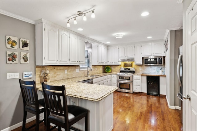 kitchen with a sink, a peninsula, beverage cooler, under cabinet range hood, and stainless steel appliances