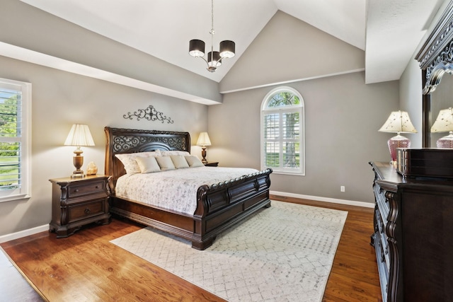 bedroom with high vaulted ceiling, multiple windows, wood finished floors, and a notable chandelier