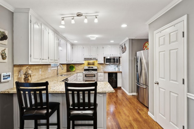 kitchen featuring appliances with stainless steel finishes, a sink, a peninsula, recessed lighting, and backsplash