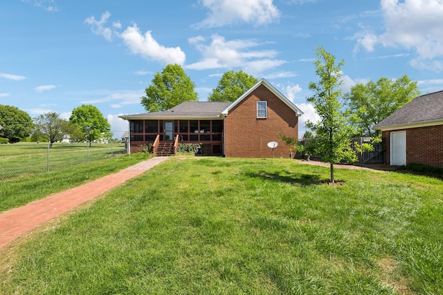 back of house featuring a sunroom, a fenced backyard, a yard, and brick siding