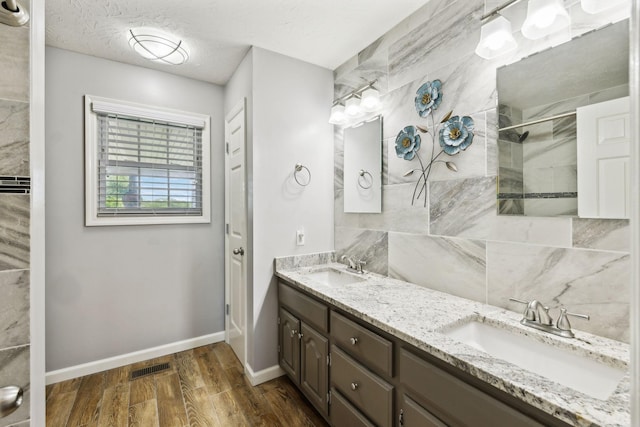full bathroom featuring double vanity, wood finished floors, a sink, baseboards, and tiled shower