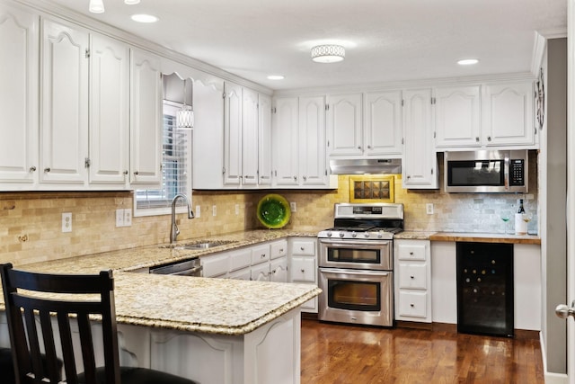 kitchen with a sink, a peninsula, under cabinet range hood, wine cooler, and stainless steel appliances
