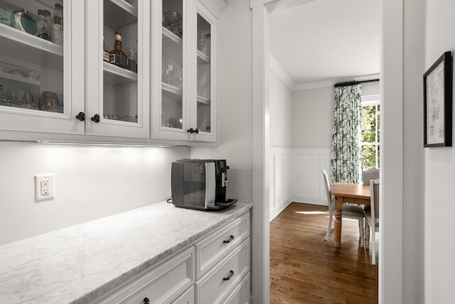 bar featuring crown molding, a wainscoted wall, a decorative wall, and dark wood-style floors